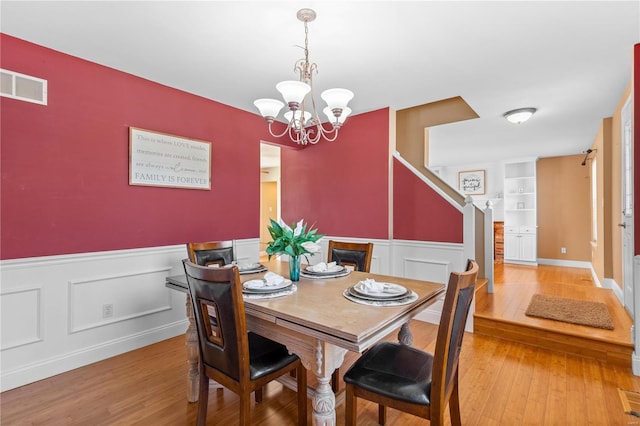 dining room with built in shelves, visible vents, light wood-style floors, wainscoting, and a chandelier