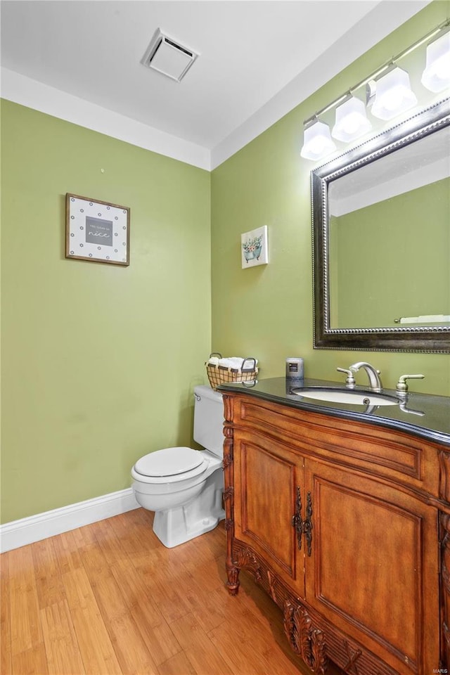 half bath featuring vanity, wood finished floors, visible vents, baseboards, and toilet