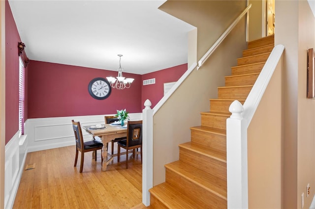 dining room with a wainscoted wall, visible vents, an inviting chandelier, stairs, and light wood-type flooring