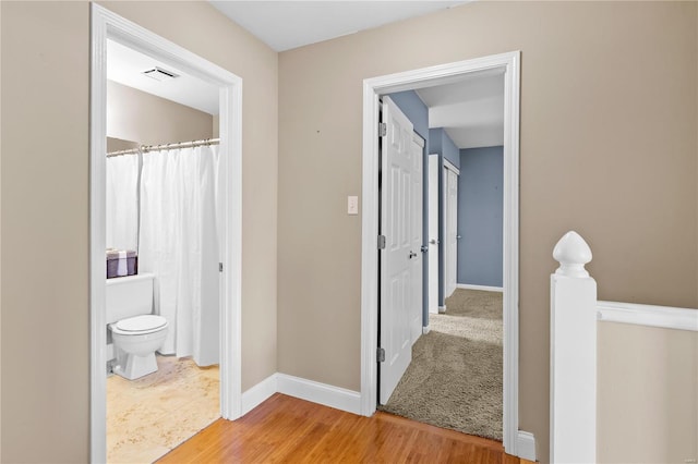 corridor featuring visible vents, an upstairs landing, baseboards, and wood finished floors