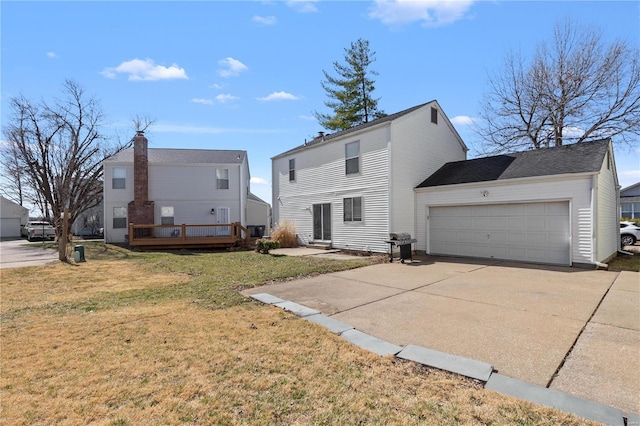 back of house with an attached garage, a lawn, driveway, and a wooden deck