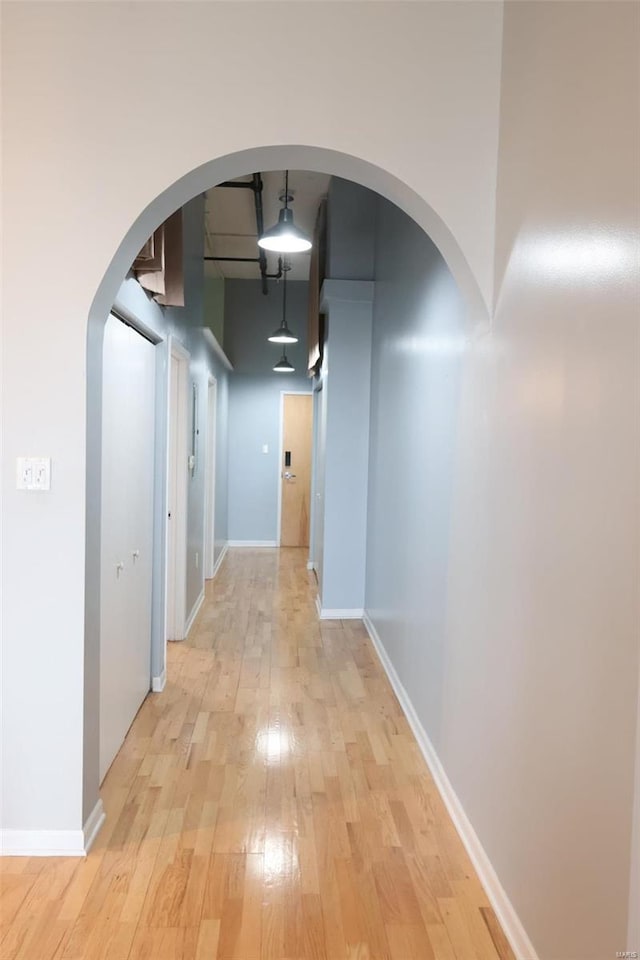 hall with light wood-type flooring, arched walkways, and baseboards