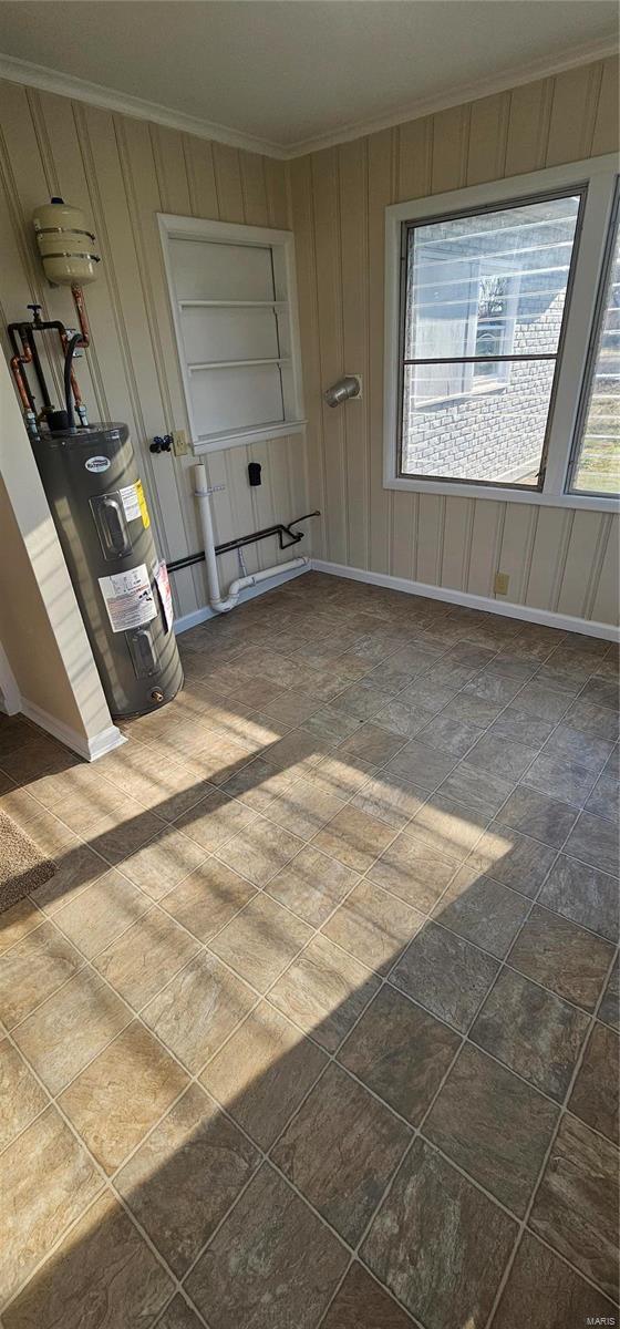 spare room featuring baseboards, electric water heater, and crown molding