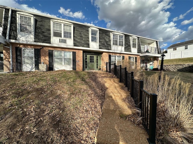 rear view of property with mansard roof, a balcony, fence, roof with shingles, and brick siding