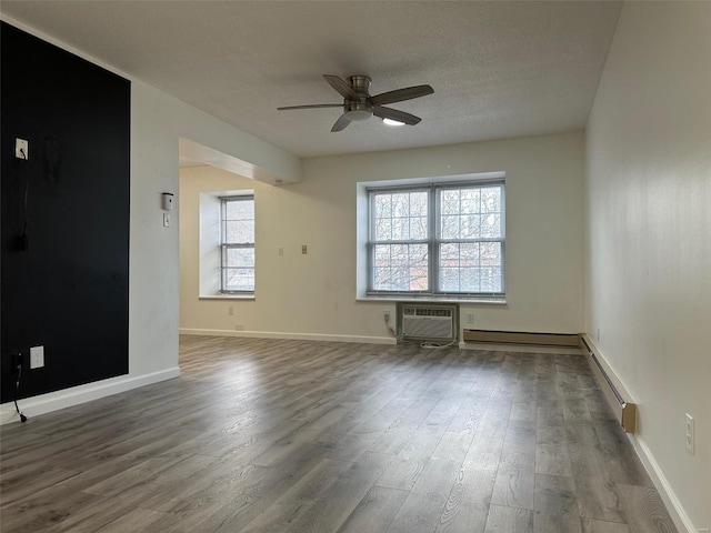 empty room featuring a textured ceiling, wood finished floors, a wall unit AC, baseboards, and ceiling fan