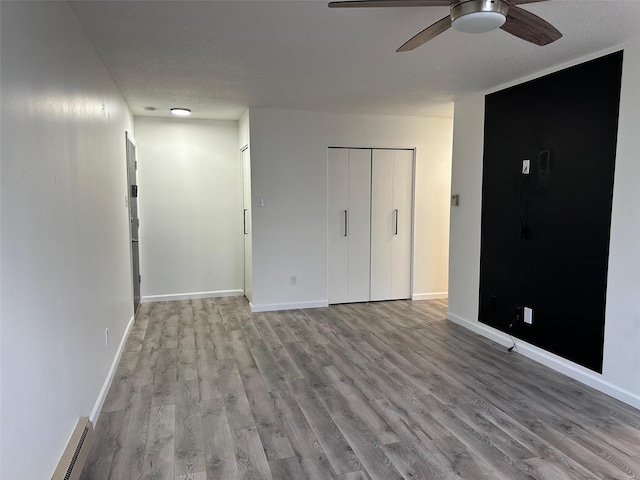 interior space featuring baseboard heating, a ceiling fan, baseboards, and wood finished floors