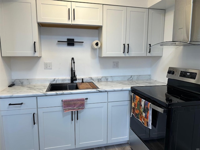 kitchen with wall chimney range hood, light stone counters, electric stove, white cabinetry, and a sink