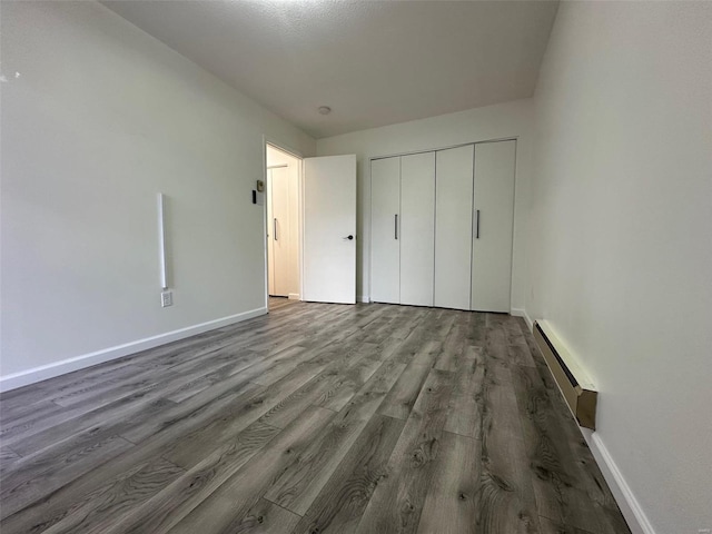 unfurnished bedroom with a closet, a baseboard heating unit, baseboards, and wood finished floors