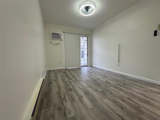 unfurnished room with a wall mounted air conditioner, a textured ceiling, wood finished floors, a baseboard radiator, and baseboards