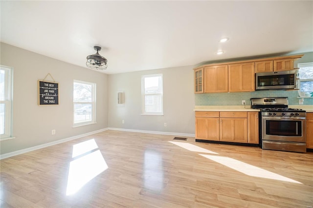 kitchen with tasteful backsplash, appliances with stainless steel finishes, light countertops, and light wood-style floors