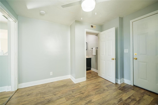 unfurnished bedroom with wood finished floors, visible vents, baseboards, ensuite bath, and ceiling fan