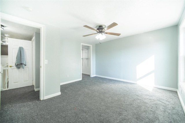 unfurnished bedroom featuring a spacious closet, baseboards, and dark colored carpet