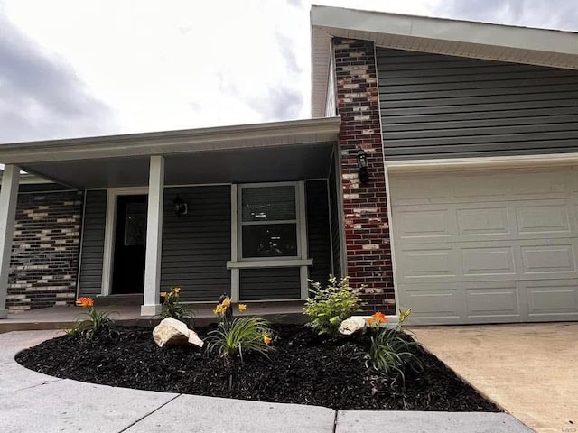 view of exterior entry with covered porch, brick siding, an attached garage, and concrete driveway