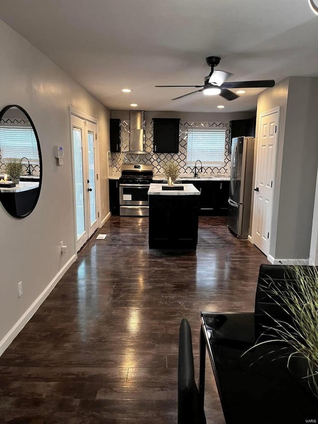 kitchen featuring tasteful backsplash, dark cabinetry, stainless steel appliances, wall chimney exhaust hood, and light countertops