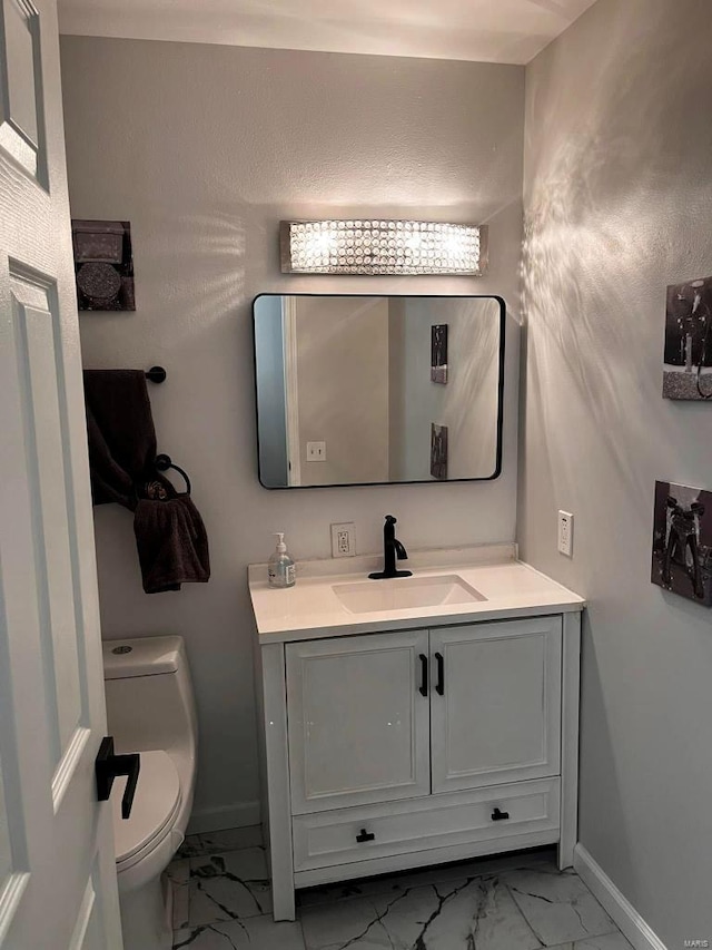 half bathroom with marble finish floor, toilet, vanity, and baseboards