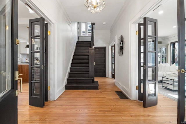 foyer entrance with crown molding, baseboards, stairway, french doors, and light wood-style floors