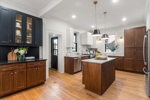 kitchen with crown molding, glass insert cabinets, decorative backsplash, light wood-style floors, and stainless steel appliances