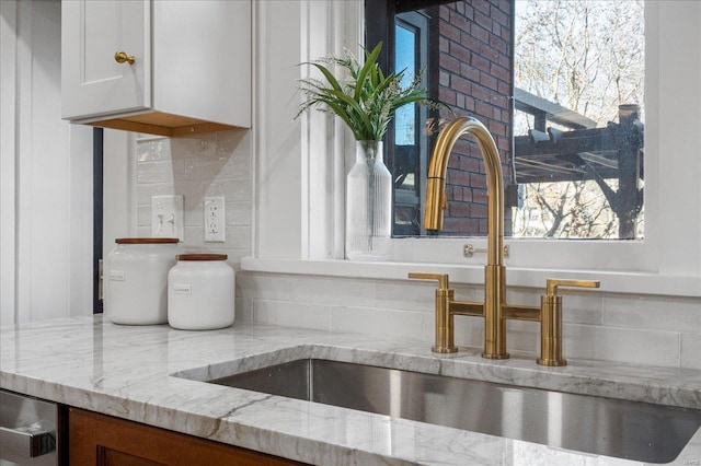 interior details featuring white cabinets, light stone counters, tasteful backsplash, and a sink