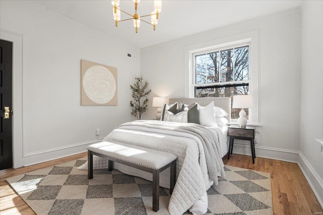 bedroom with a notable chandelier, wood finished floors, visible vents, and baseboards