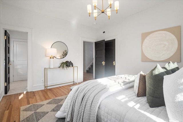 bedroom featuring visible vents, a notable chandelier, wood finished floors, and baseboards