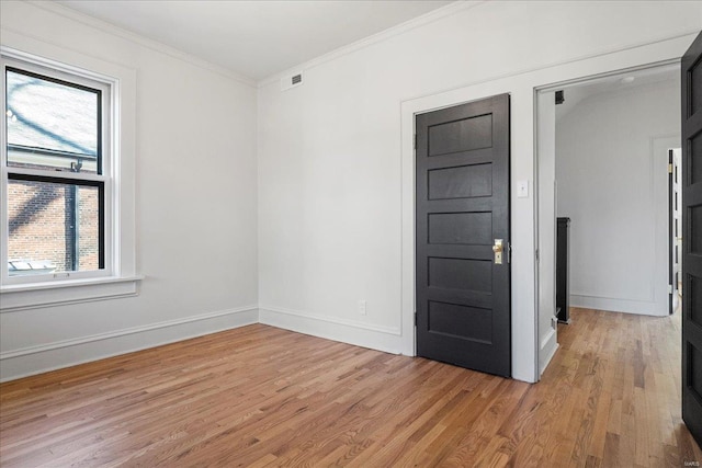 spare room with visible vents, baseboards, light wood finished floors, and ornamental molding