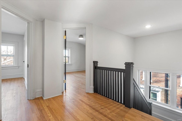 corridor with baseboards, light wood-type flooring, an upstairs landing, and a healthy amount of sunlight