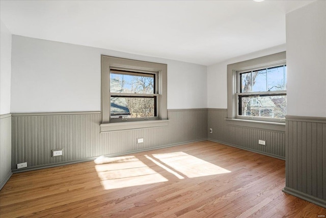 empty room with wood finished floors, a wainscoted wall, and a wealth of natural light