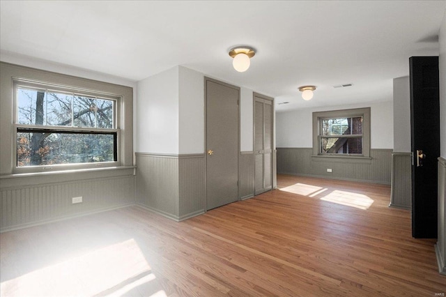 empty room featuring visible vents, wood finished floors, and a wainscoted wall