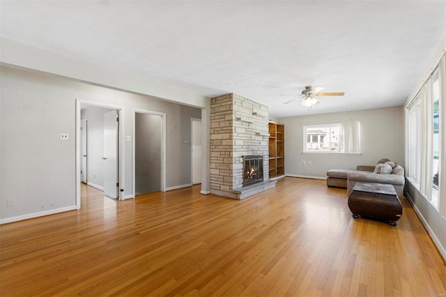 unfurnished living room featuring a ceiling fan, light wood-type flooring, a stone fireplace, and baseboards