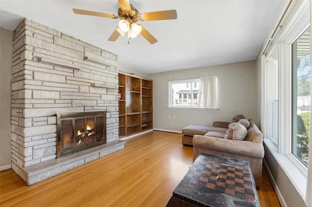 living area featuring ceiling fan, a stone fireplace, wood finished floors, and baseboards