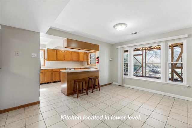 kitchen with light tile patterned flooring, a peninsula, visible vents, light countertops, and a kitchen bar