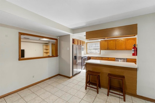 kitchen with stainless steel appliances, a breakfast bar, a peninsula, light countertops, and brown cabinetry