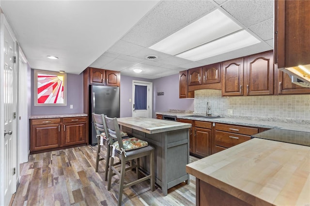 kitchen with light wood finished floors, butcher block counters, freestanding refrigerator, a sink, and backsplash