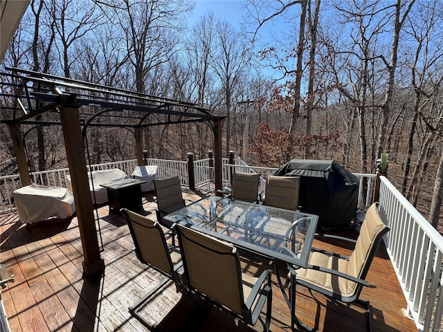 wooden terrace featuring outdoor dining space, a grill, a wooded view, and a pergola