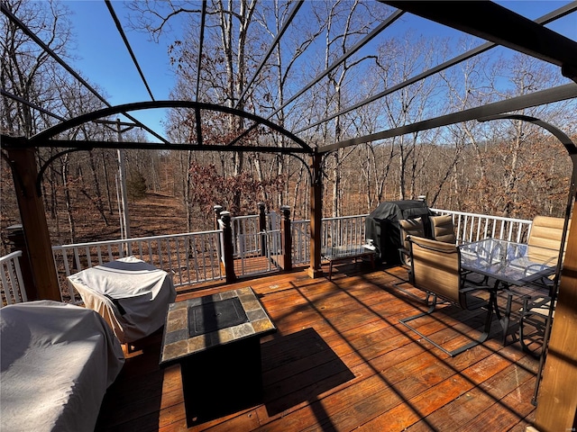 deck with outdoor dining space, grilling area, and a wooded view