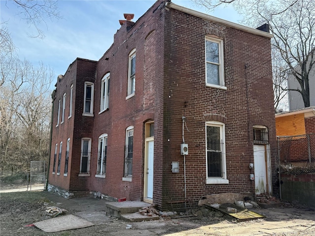 view of side of home with brick siding, entry steps, a chimney, and fence