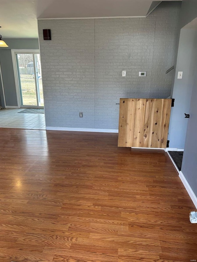 unfurnished room with baseboards, wood finished floors, and brick wall