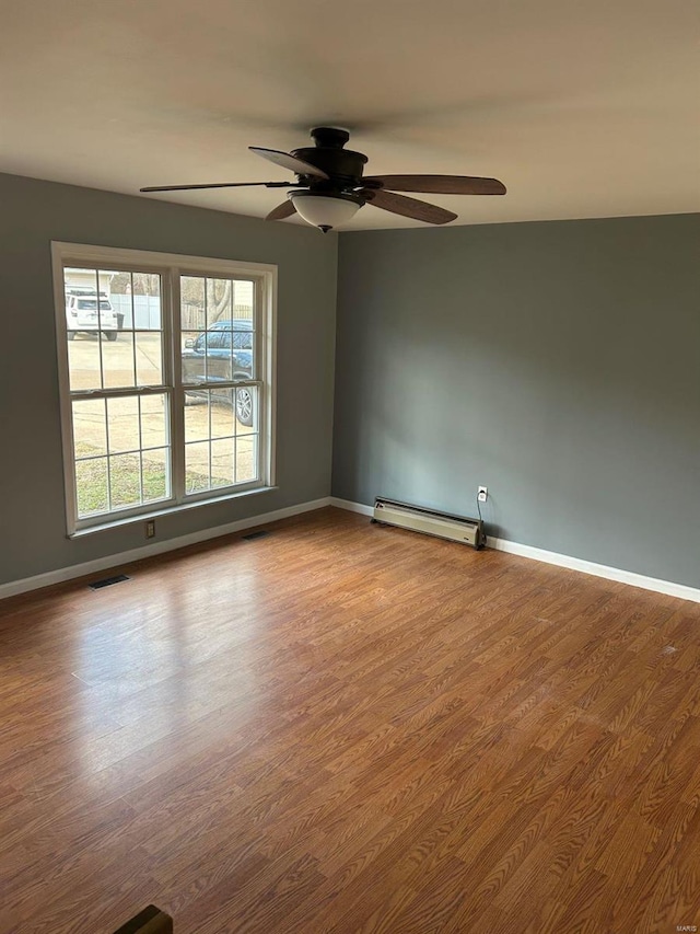 spare room with visible vents, a ceiling fan, wood finished floors, baseboards, and baseboard heating