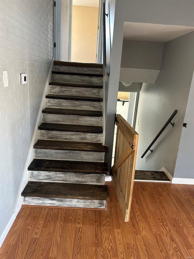 stairs with baseboards, wood finished floors, and brick wall