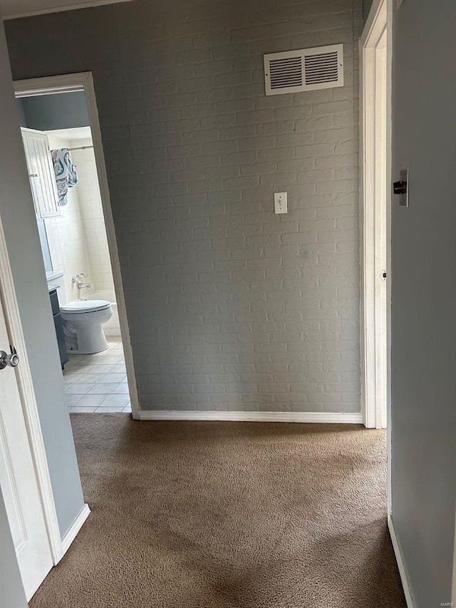 corridor featuring tile patterned flooring, visible vents, brick wall, baseboards, and carpet flooring