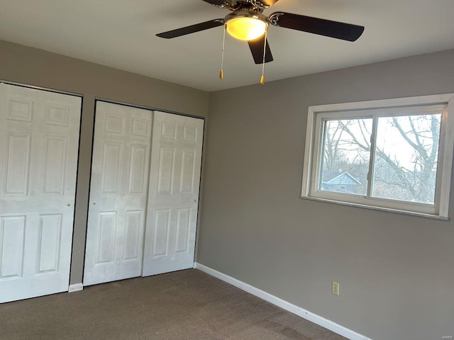 unfurnished bedroom with multiple closets, dark carpet, baseboards, and ceiling fan