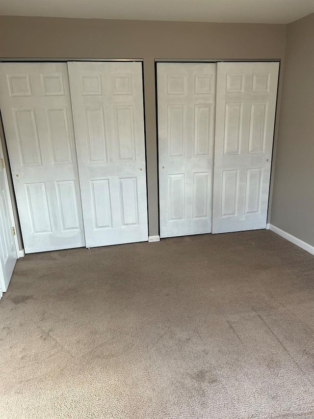 unfurnished bedroom featuring carpet, multiple closets, and baseboards