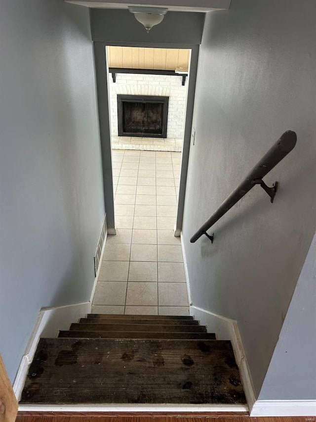 stairs with tile patterned flooring, visible vents, a brick fireplace, and baseboards