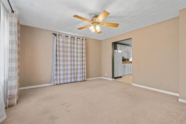 spare room with baseboards, light carpet, and a ceiling fan