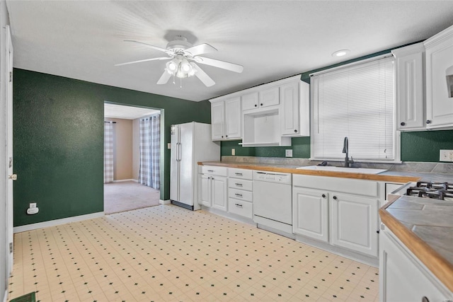 kitchen with white appliances, a ceiling fan, baseboards, a sink, and white cabinetry