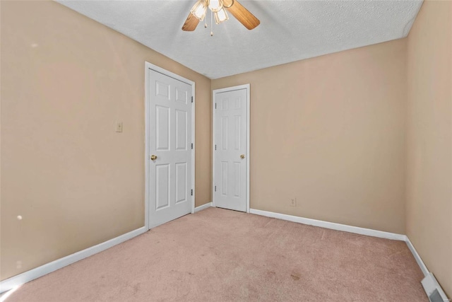 empty room with light carpet, a textured ceiling, a ceiling fan, and baseboards