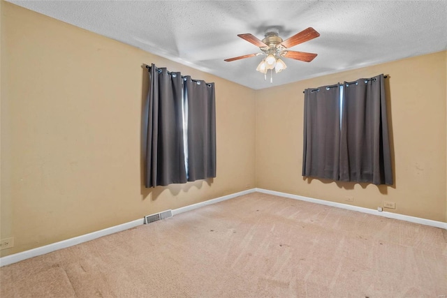 carpeted empty room with a ceiling fan, baseboards, visible vents, and a textured ceiling