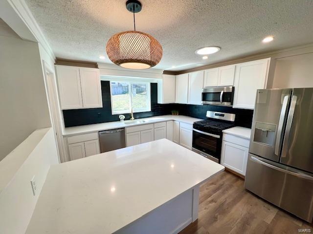 kitchen with stainless steel appliances, wood finished floors, white cabinets, and light countertops