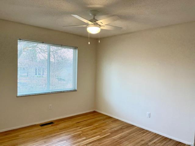 empty room featuring visible vents, a textured ceiling, light wood-style floors, baseboards, and ceiling fan