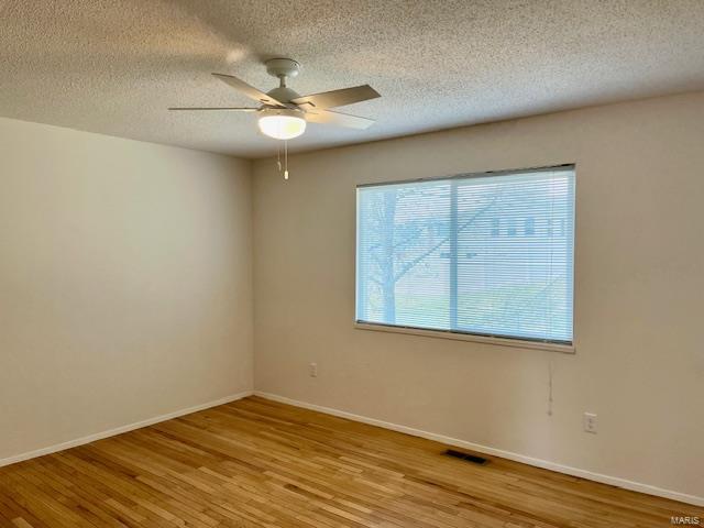 unfurnished room featuring a ceiling fan, wood finished floors, visible vents, and baseboards